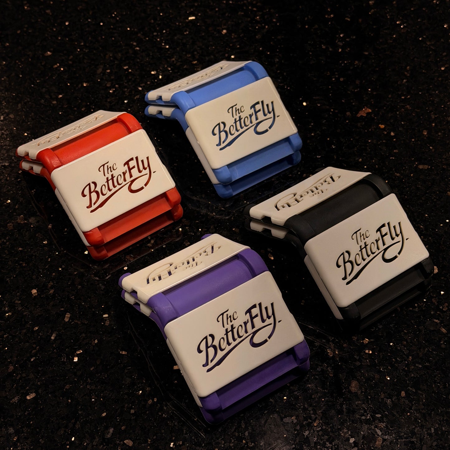 Four 'The BetterFly' products in different colors on a dark textured background