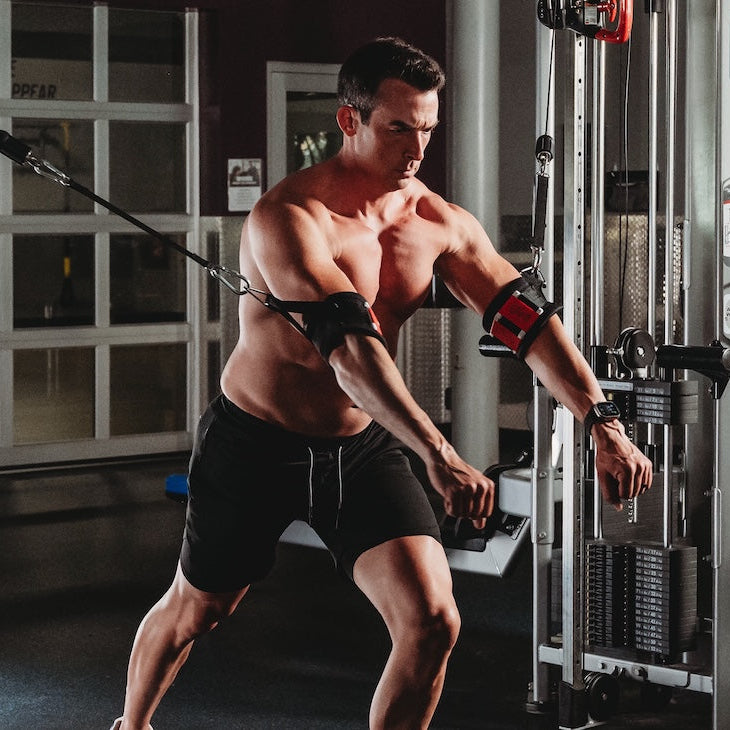 Muscular man using cable arm cuffs for chest fly workout in gym